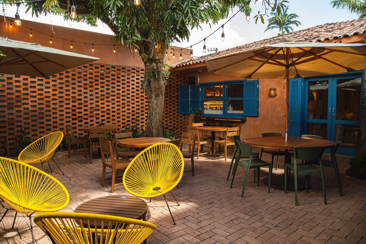 Área externa do café com mesas e cadeiras amarelas